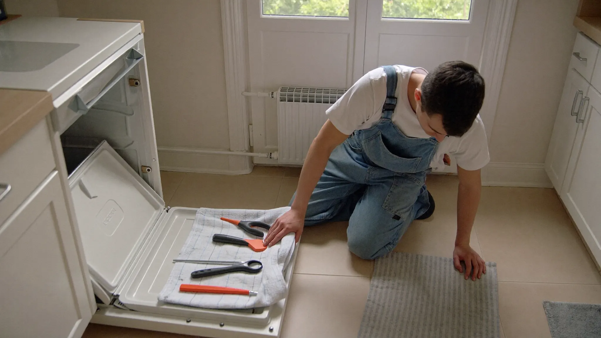Appliance repair technician kneeling beside an open dishwasher in a home kitchen