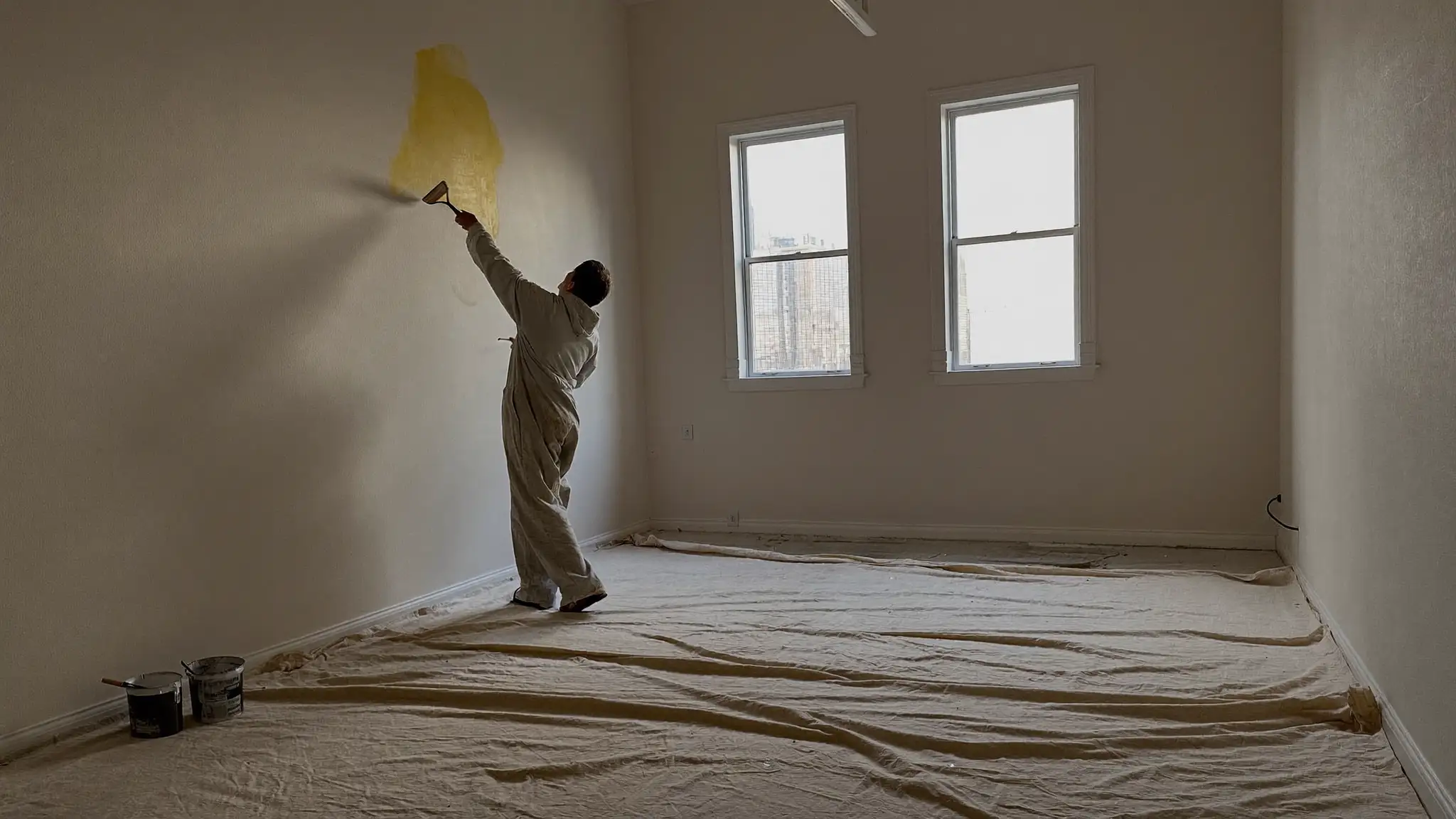 Painter in coveralls rolling white paint onto an interior wall