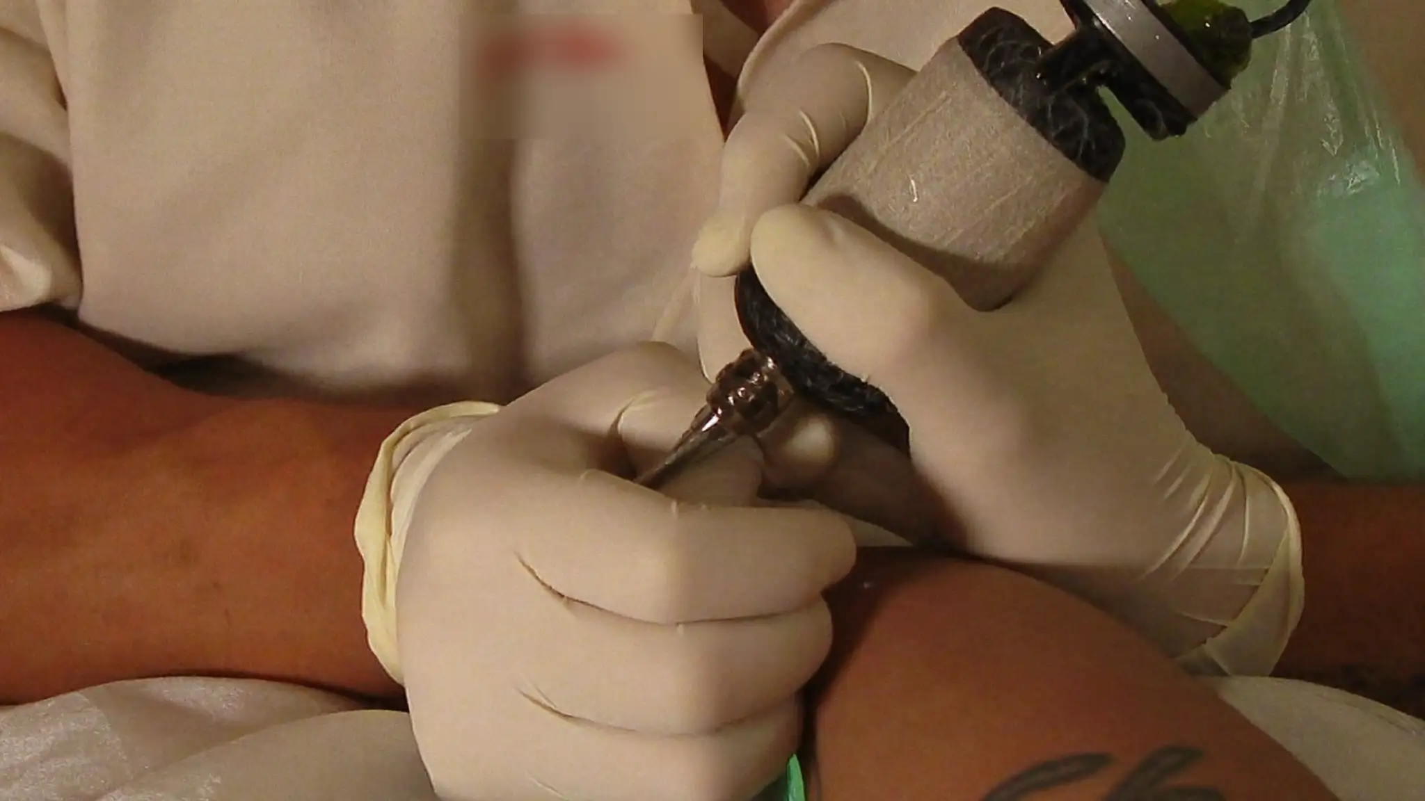 Tattoo artist's gloved hands tattooing a client's forearm at a studio station