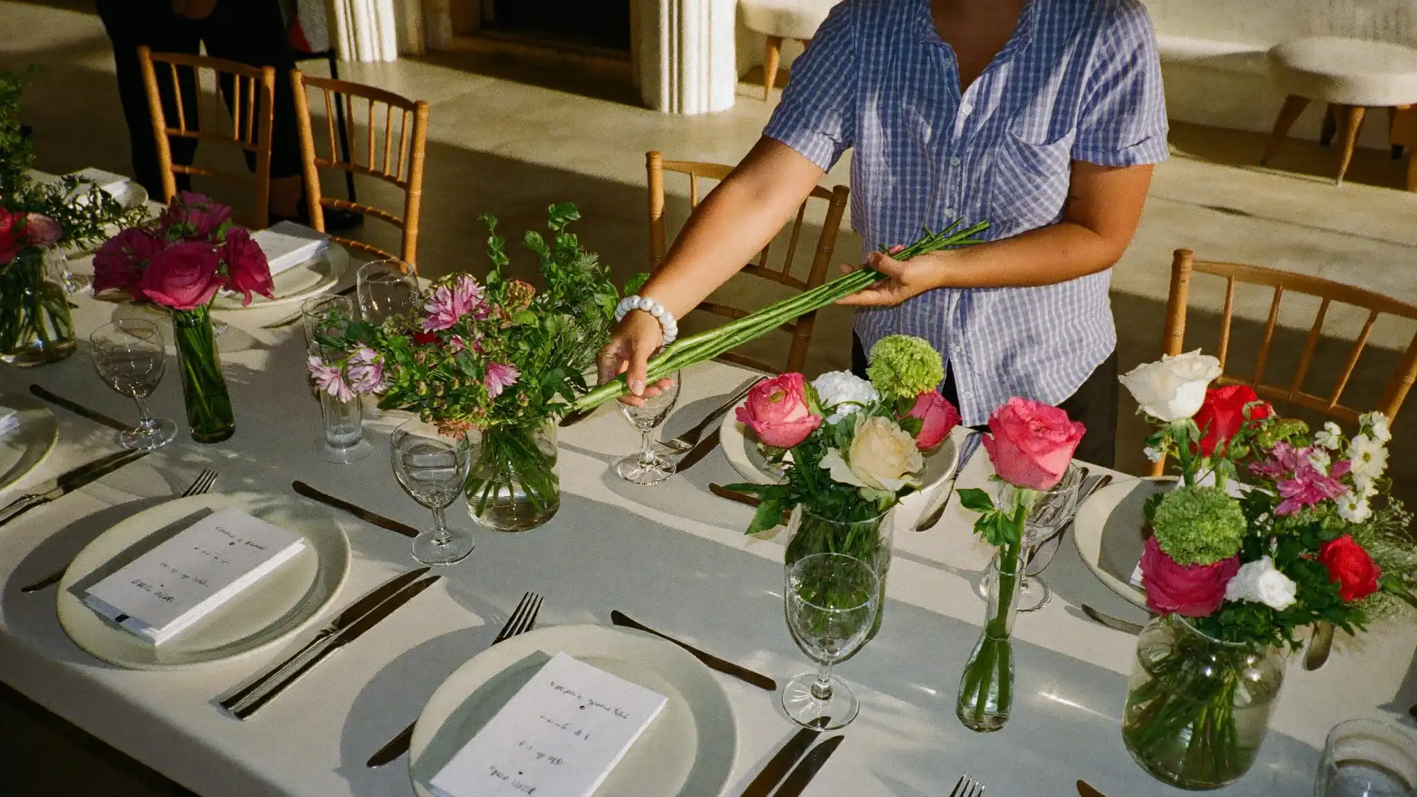 Wedding planner arranging floral centerpieces on a reception table before the ceremony