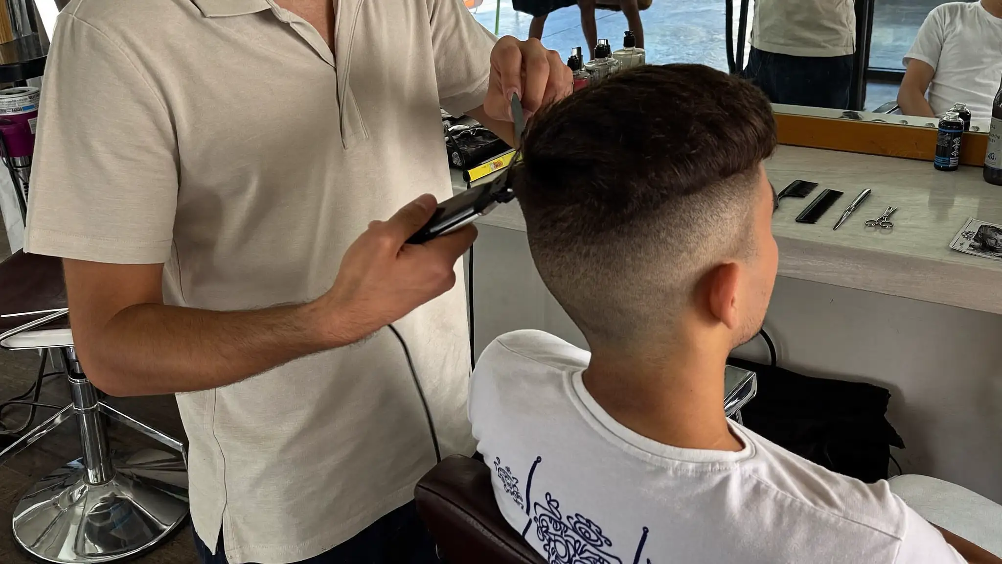 Barber using clippers to trim a seated client's hair in a barbershop chair
