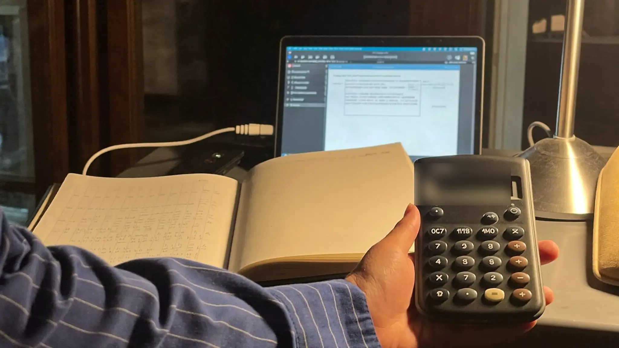 Bookkeeper's hand using a calculator beside an open ledger notebook