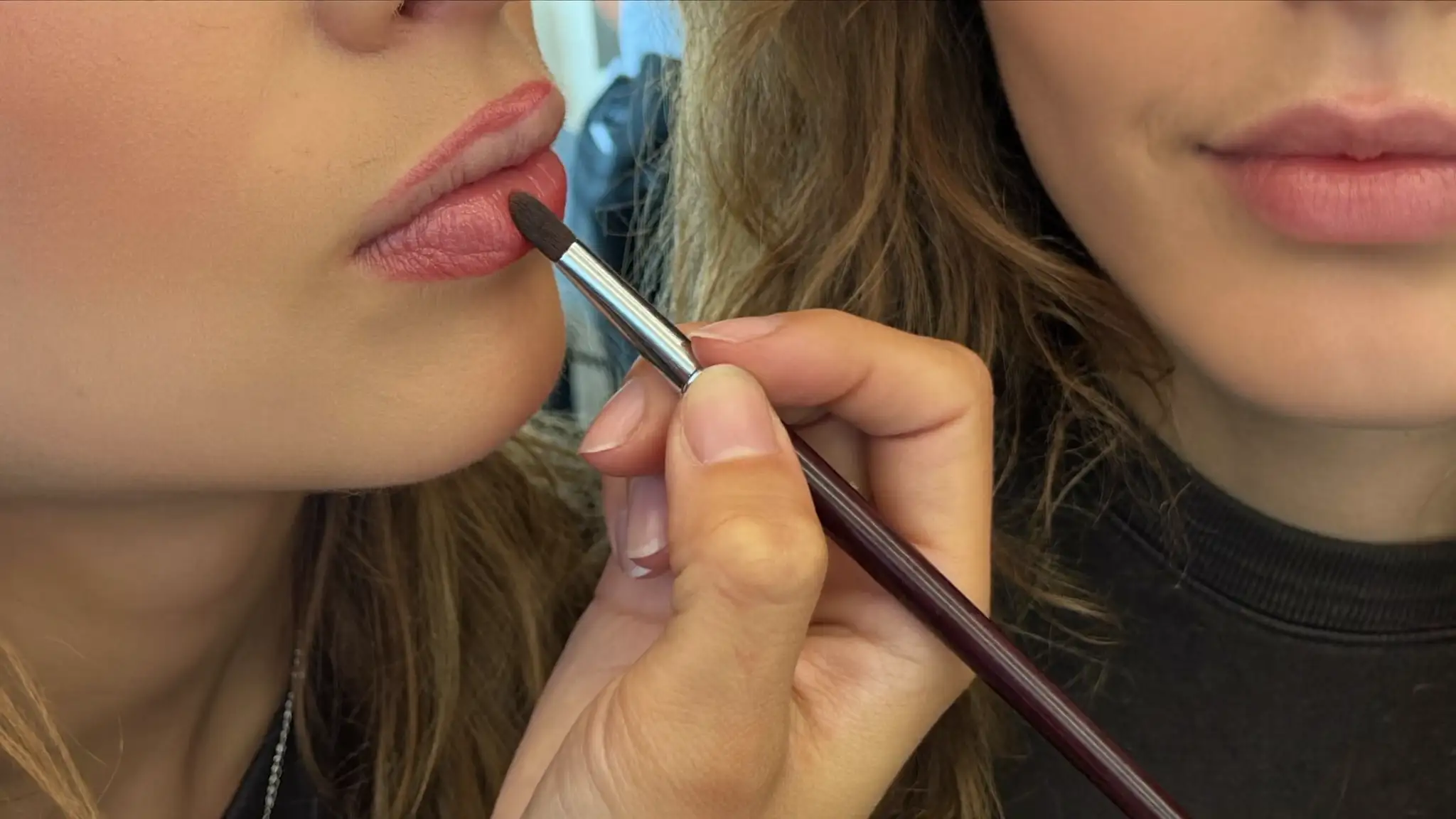Makeup artist applying lip color to a seated client