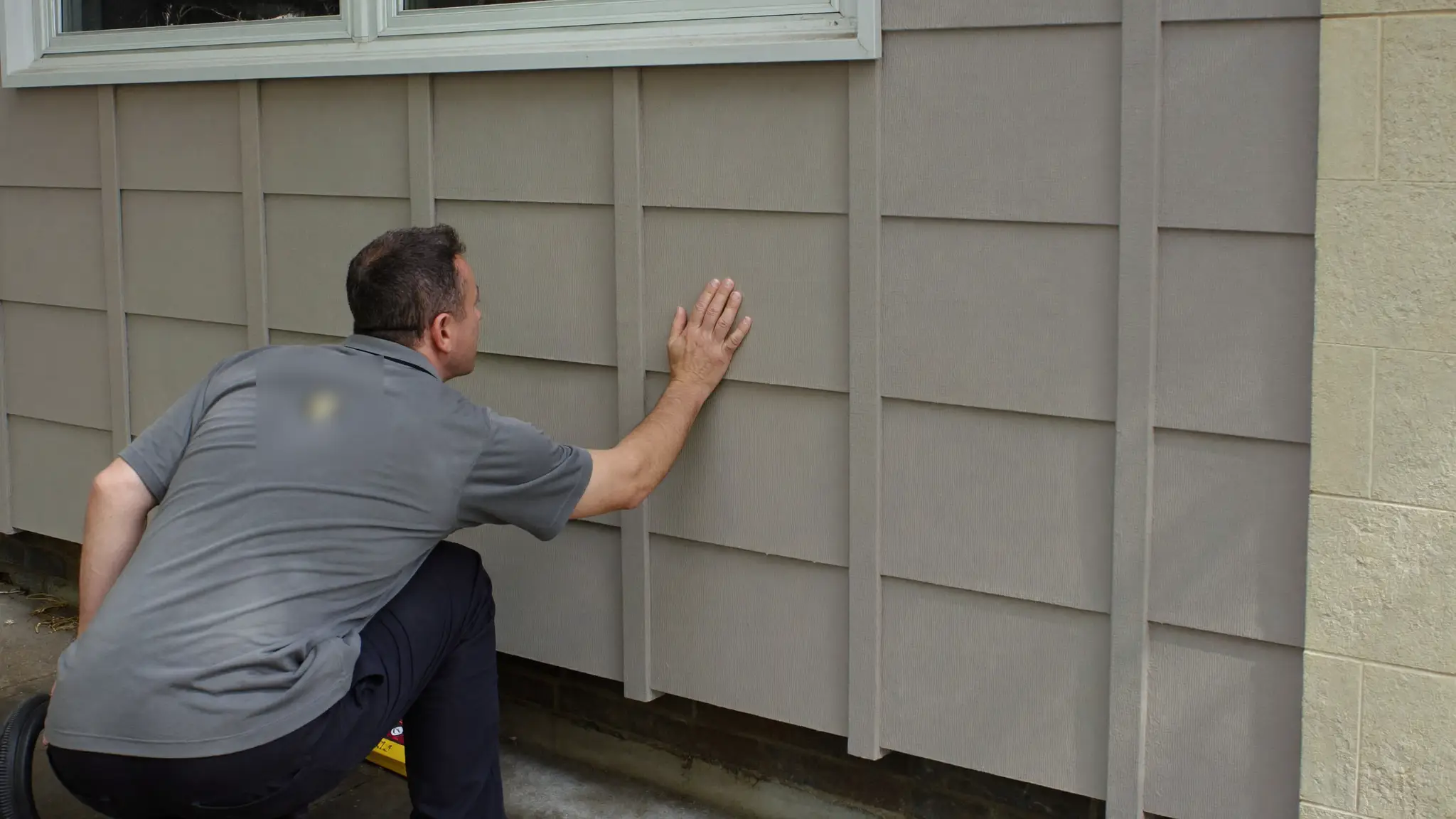 Pest control technician inspecting a home's exterior foundation and siding