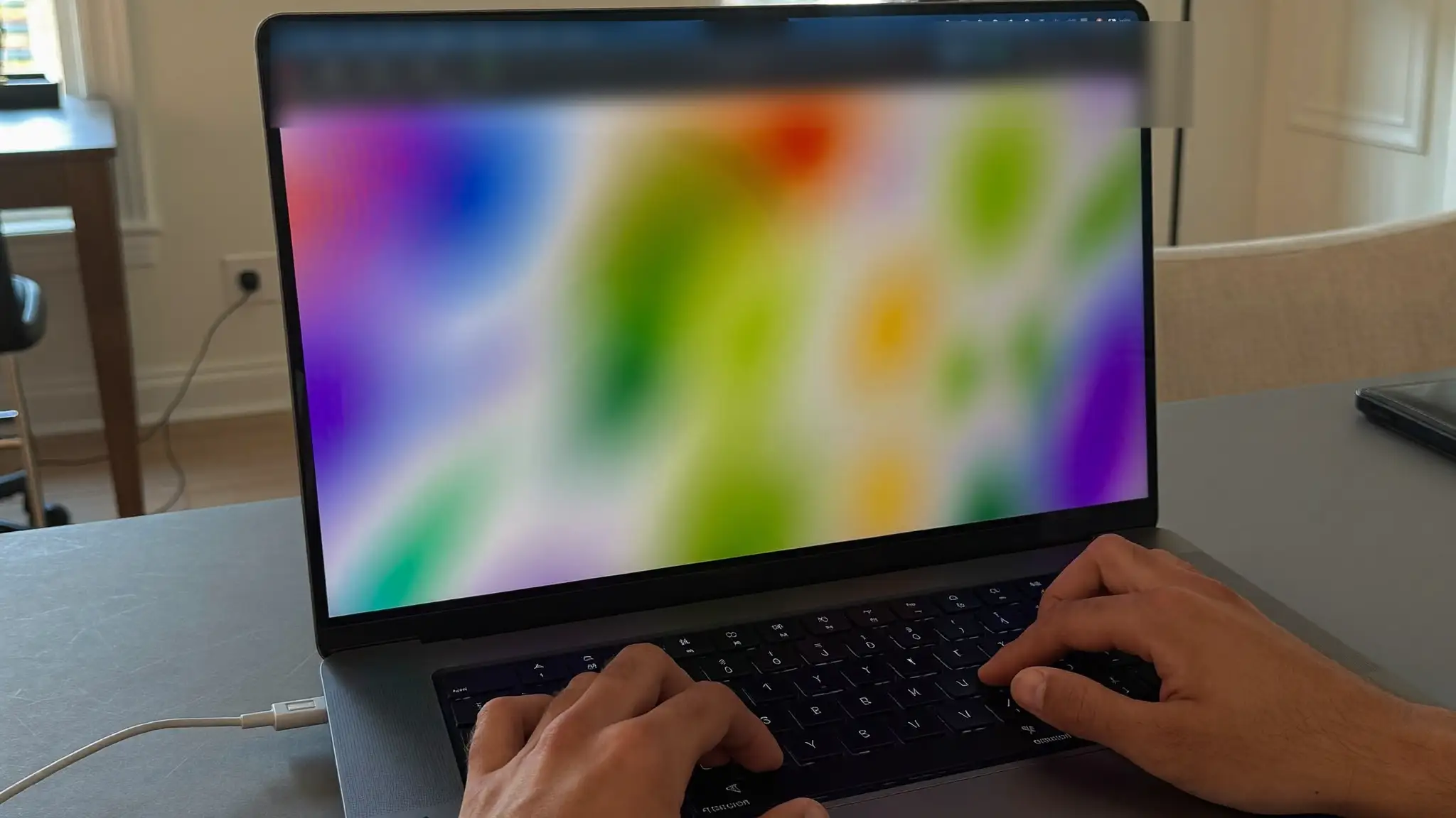 Web designer's hands typing on a laptop showing a blurred abstract colorful layout